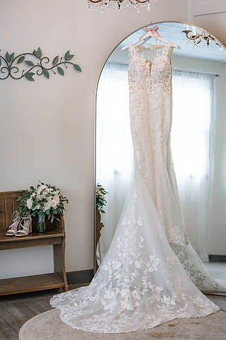 Dress hanging in tall glamorous full length mirror with florals and bridal shoes off to the side