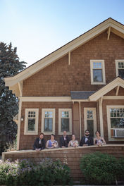 Wedding party smiling at the camera standing on the porch of a wooden house