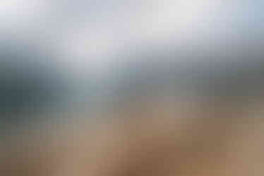 A couple stands on a rocky trail in the Canadian Rockies, the woman lifting her foot playfully as they look at each other, surrounded by towering mountains and a tranquil lake. With Alberta wedding photographer taking photo of them.