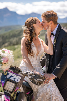 Close-up of the bride and groom kissing as the bride sits on her dirt bike and the groom stands in front of her with Rocky Mountain views behind them, photographed by a Cochrane wedding photographer.