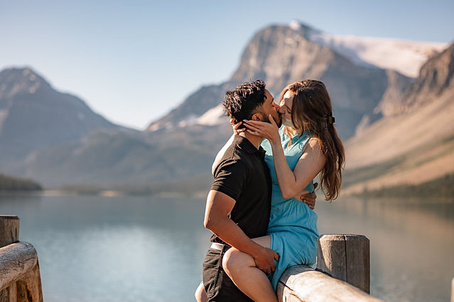 couple sharing a kiss on a wooden dock at Bow Lake with mountains and calm water behind them 