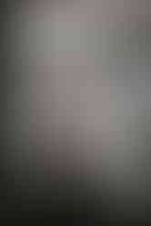 A reflection shot of the groom doing up his grey vest in the mirror.