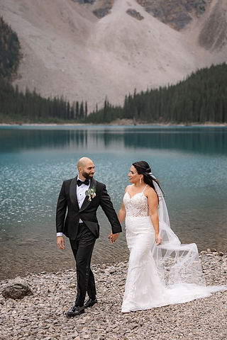 Bride and groom strolling along the shoreline during a Moraine Lake wedding with family