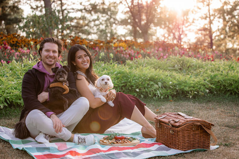 couple smile and hold their dogs at their picnic engagement
