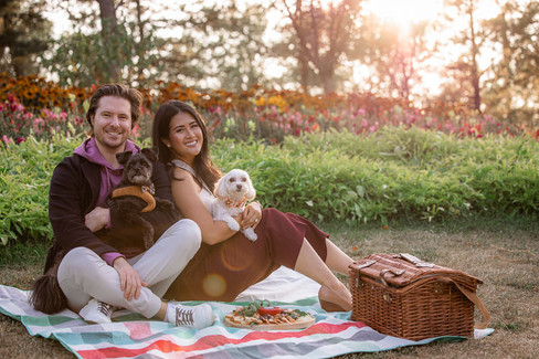 couple smile and hold their dogs at their picnic engagement 