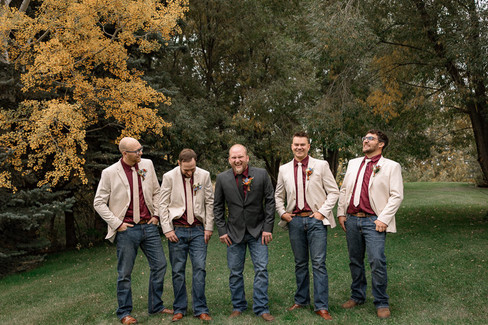 Groom and groomsmen laughing together in casual rustic wedding attire at the Strathmore wedding venue surrounded by fall trees and relaxed countryside wedding vibes.