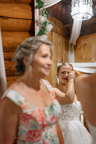 The mother smiles proudly at her daughter while the bride wipes away her tears of joy reflected in the mirror