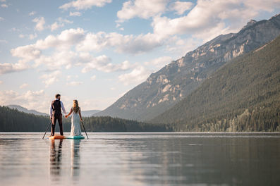 Bride and groom on paddleboards surrounded by mountains on a calm lake on their Crowsnest Pass wedding day