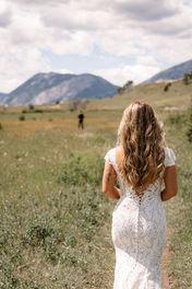 Bride in a lace wedding dress walking through a grassy field in Crowsnest Pass with mountains in the background. on their Crowsnest Pass wedding day