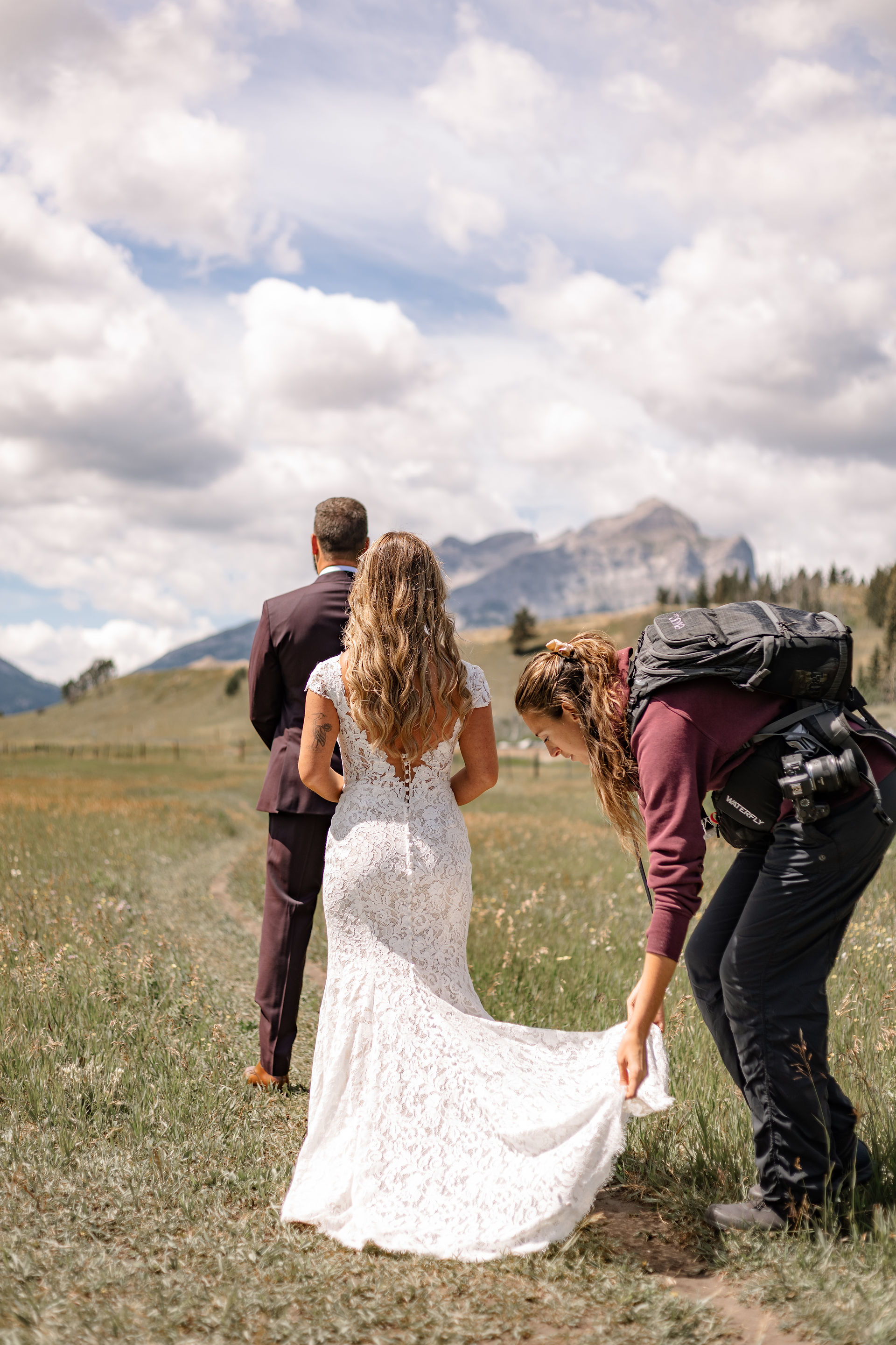 Photographer adjusting the bride's dress while the couple stands together outdoors
