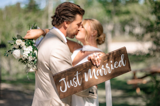 Bride and groom sharing a kiss beside a Just Married sign captured by a mountain wedding photographer in Alberta