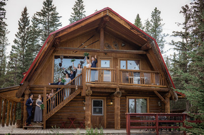 Front of log cabin with whole bridal party lined up on the stairs celebrating