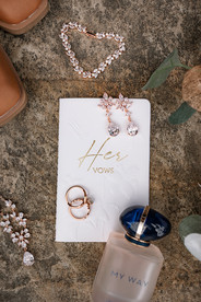 A vertical shot of detailed shot of the bride’s cowgirl boots, vow book, jewelry, bouquet, and perfume bottle.