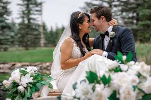 Bride and groom sitting in canoe with white and green florals surrounding them, holding hands