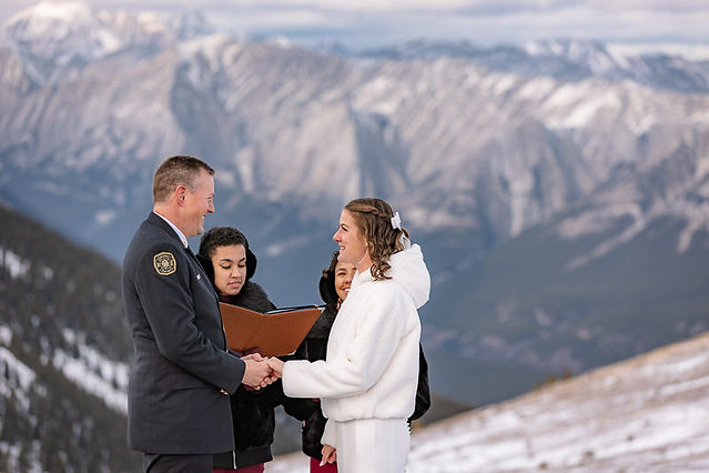 Bride and groom holding hands during their intimate helicopter elopement ceremony with snowy peaks behind them.