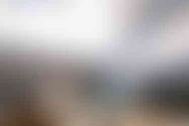 A couple stands arm in arm on a mountain ledge in the Canadian Rockies, overlooking a calm tranquil lake surrounded by rugged peaks and golden fall foliage under a soft cloudy sky