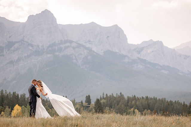 Bride and groom embrace in an open field with sweeping Rocky Mountain views, showcasing the breathtaking scenery that makes Canmore wedding venues so unforgettable.