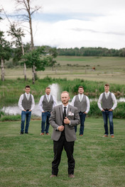 The groom and groomsmen pose on the lawn at Diamond in the Rough, with the groom up front and a fountain visible behind them.