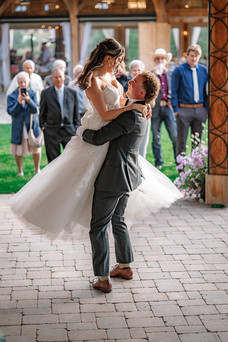 Groom joyfully lifting the bride during their first dance under a wooden gazebo while family and friends watch in the background , captured by a Southern Alberta Wedding Photographer.