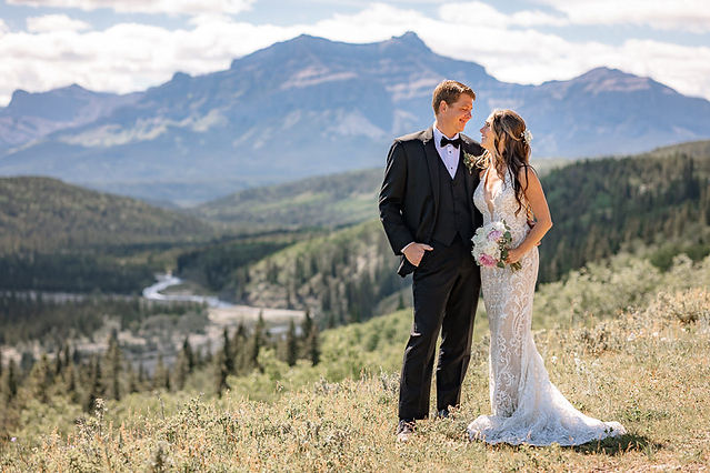 Bride and groom standing together on a mountain overlook with the Canadian Rockies behind them after their ceremony, photographed by a Cochrane wedding photographer.