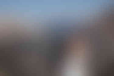 groom hugs bride from behind they both smile on top of mountains