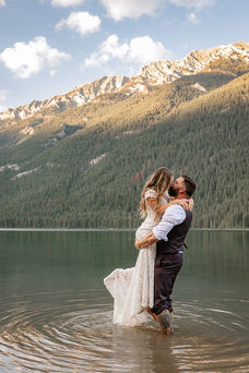 Bride and groom embracing while standing in a calm mountain lake on their Crowsnest Pass wedding day