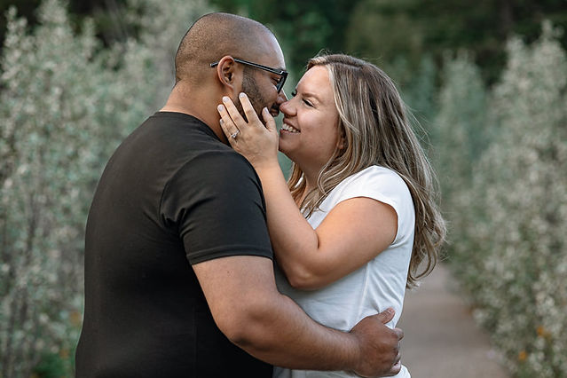 Couple kissing with their teeth amongst sage coloured brush 