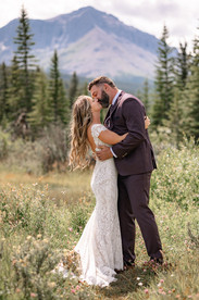 Bide and groom sharing an embrace during an outdoor wedding with mountains in the background on their Crowsnest Pass wedding day