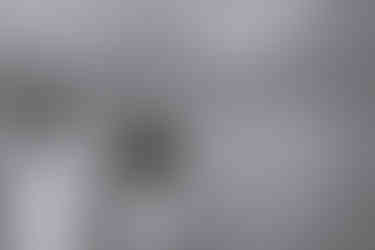 A couple holds hands while walking along the edge of Bow Lake, with towering peaks rising behind them under soft, overcast light.