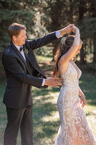 Groom spinning the bride as she twirls in her lace wedding dress in a forest setting at one of the beautiful Cochrane wedding venues.