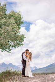 Bride and groom standing together beneath a tree with sweeping Southern Alberta Wedding Photographer with mountain views. on their Crowsnest Pass wedding day