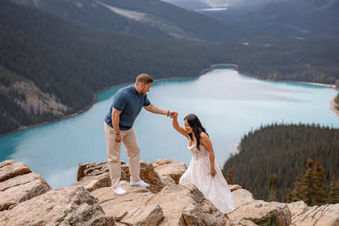 A couple climbs the rocky trail at Peyto Lake as the man gently helps the woman with each step, with water and two towering mountains stretching behind them — capturing a moment of teamwork and love in a breathtaking alpine setting.