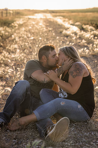 Engagement photo sitting in field kiss pose