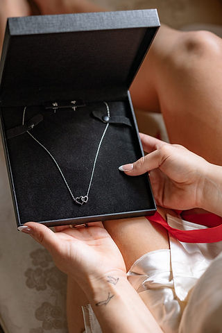 A close-up of the bride’s hands holding a black gift box with two overlapping hearts inside and a red ribbon visible on the side