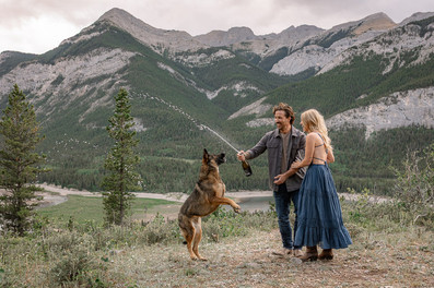 Couple celebrating with their dog after a Kananaskis surprise proposal, surrounded by mountain scenery.