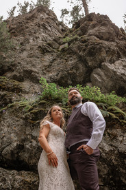 Bride and groom standing together beneath rugged rock formations in Fernie, surrounded by natural scenery on their Crowsnest Pass wedding day