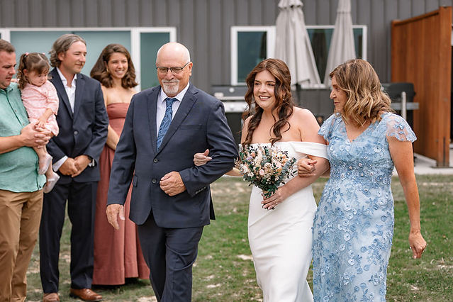 Bride walking with her parents while the guests watch in the background during her Bow Lake elopement    