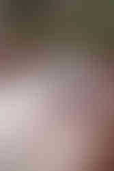 From behind, a couple kisses on red rocks with a rushing river in Waterton National Park during their engagement photoshoot.