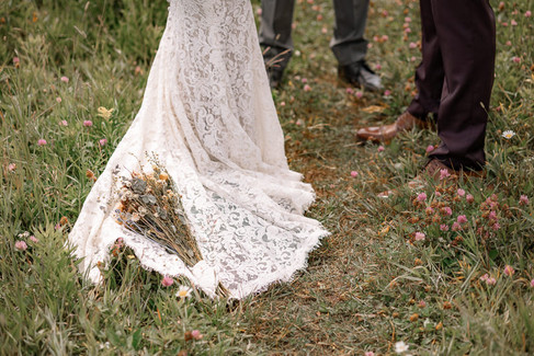 Close up detail of the bride's lace wedding dress trailing along the grass on their Crowsnest Pass wedding day