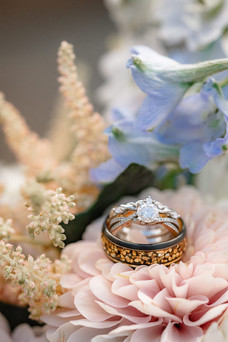 A Canmore wedding photographer captures the wedding bands and engagement ring resting among soft pastel flowers, highlighting the intricate details and romantic styling of the couple's wedding day.