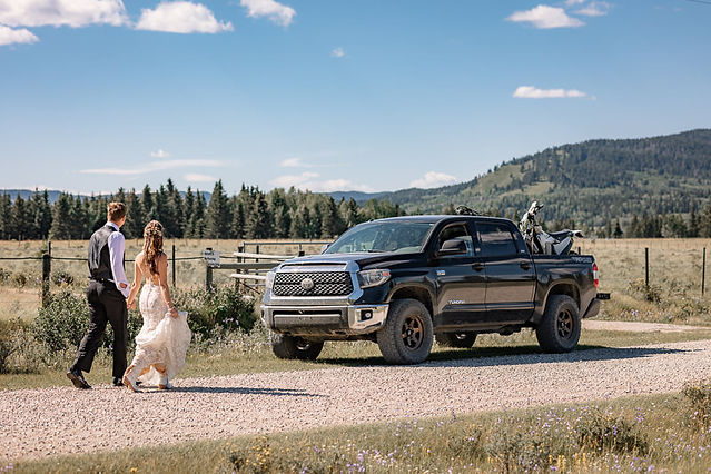 Bride and groom walking together along a country road toward a pickup truck during their wedding day at one of the scenic Cochrane wedding venues.