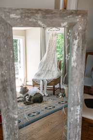 Mirror reflection of a lace wedding dress hanging by a window with cowgirl boots below and a dog in a tutu resting nearby during getting-ready moments for The Crossing at Ghost River elopement.