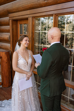 Bride and groom standing outside a rustic cabin reading their vows with forest views during a fall wedding in Bragg Creek.
