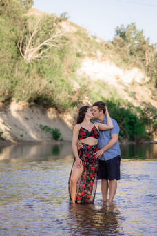 Sean embraces Samina from behind and kisses her while both standing in the river