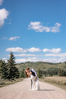 Groom dipping the bride for a kiss on a gravel road with rolling countryside views at one of the scenic Cochrane wedding venues.