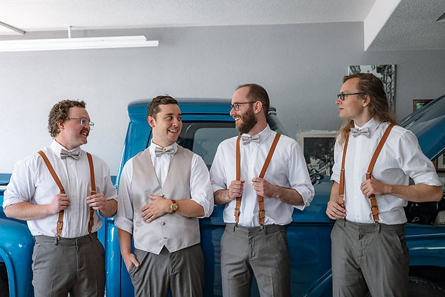 Groom laughing and smiling with groomsmen with blue truck in background