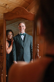 A woman standing beside the groom in front of a mirror, both smiling while getting ready at a Coutts Centre wedding.