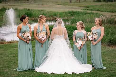 The bride stands with her bridemaids at the Diamond in the Rough showing casing her flowing gown  in front of the fountain