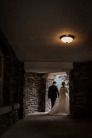 bride and groom walk hand in hand in stone wall archway
