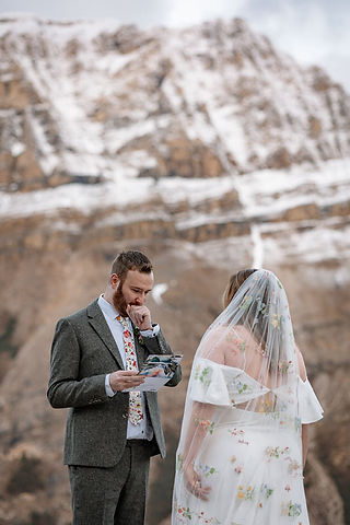 groom saying vows in front of snowy mountains